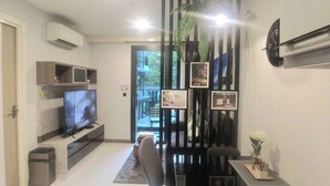 A modern living room with a flat-screen TV, a black entertainment unit, a small table with a vase, and a decorative plant. - B307 - 1 Bedroom Condo Pool View Near Ao Nang Beach (Krabi)