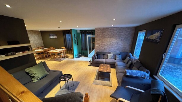 A modern living room with a sofa, armchairs, and a coffee table. There is a dining area with a table and chairs. The room has a large window and a view of the outdoors. - Chalet Iskar Borovets (Samokov)
