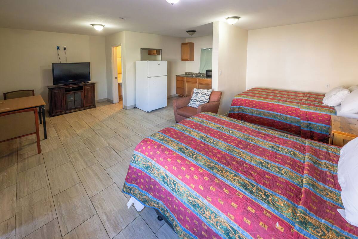 Una habitación de hotel con cama, escritorio, televisor, refrigerador y kitchenette.