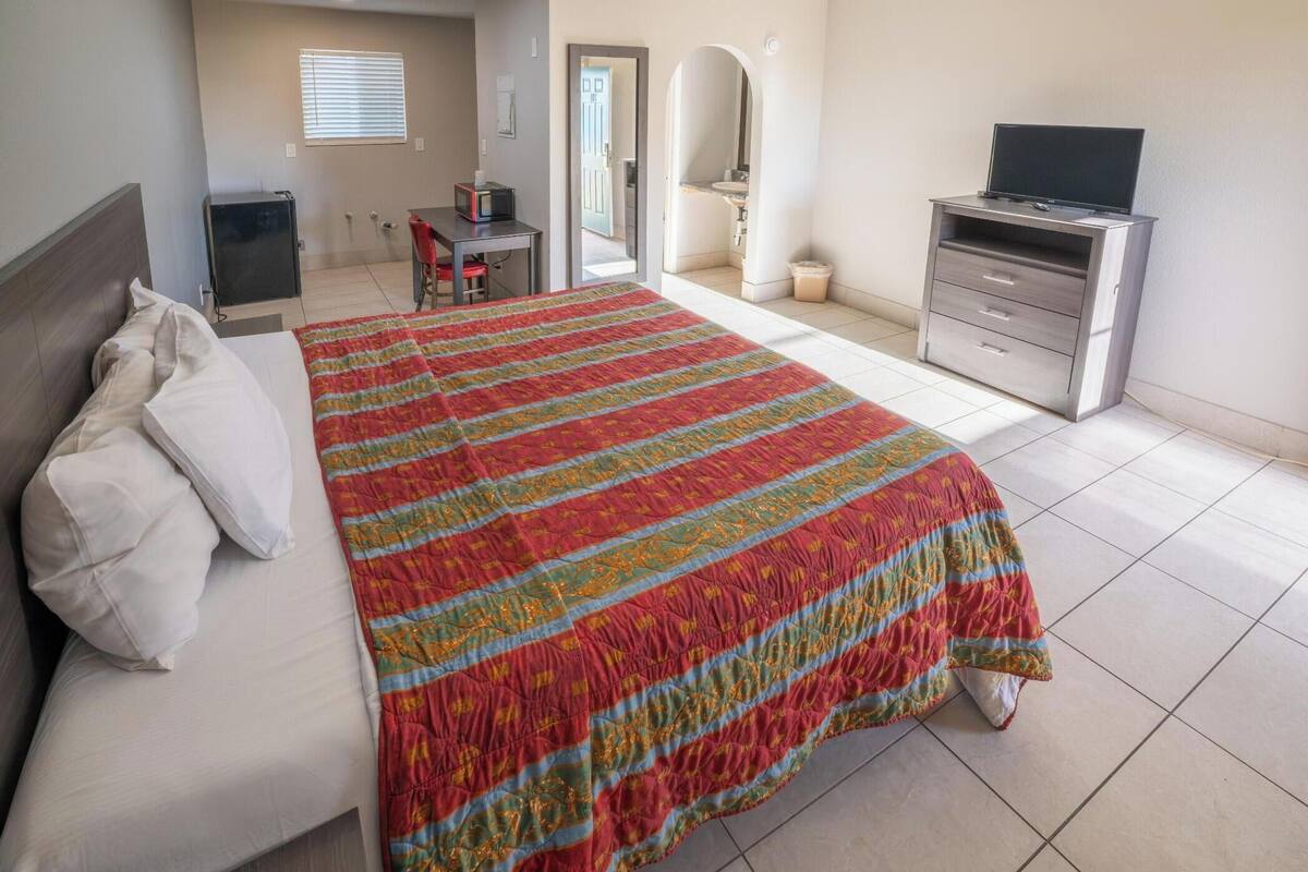 Habitación de hotel con cama, escritorio, televisor y baño visible a través de un arco.