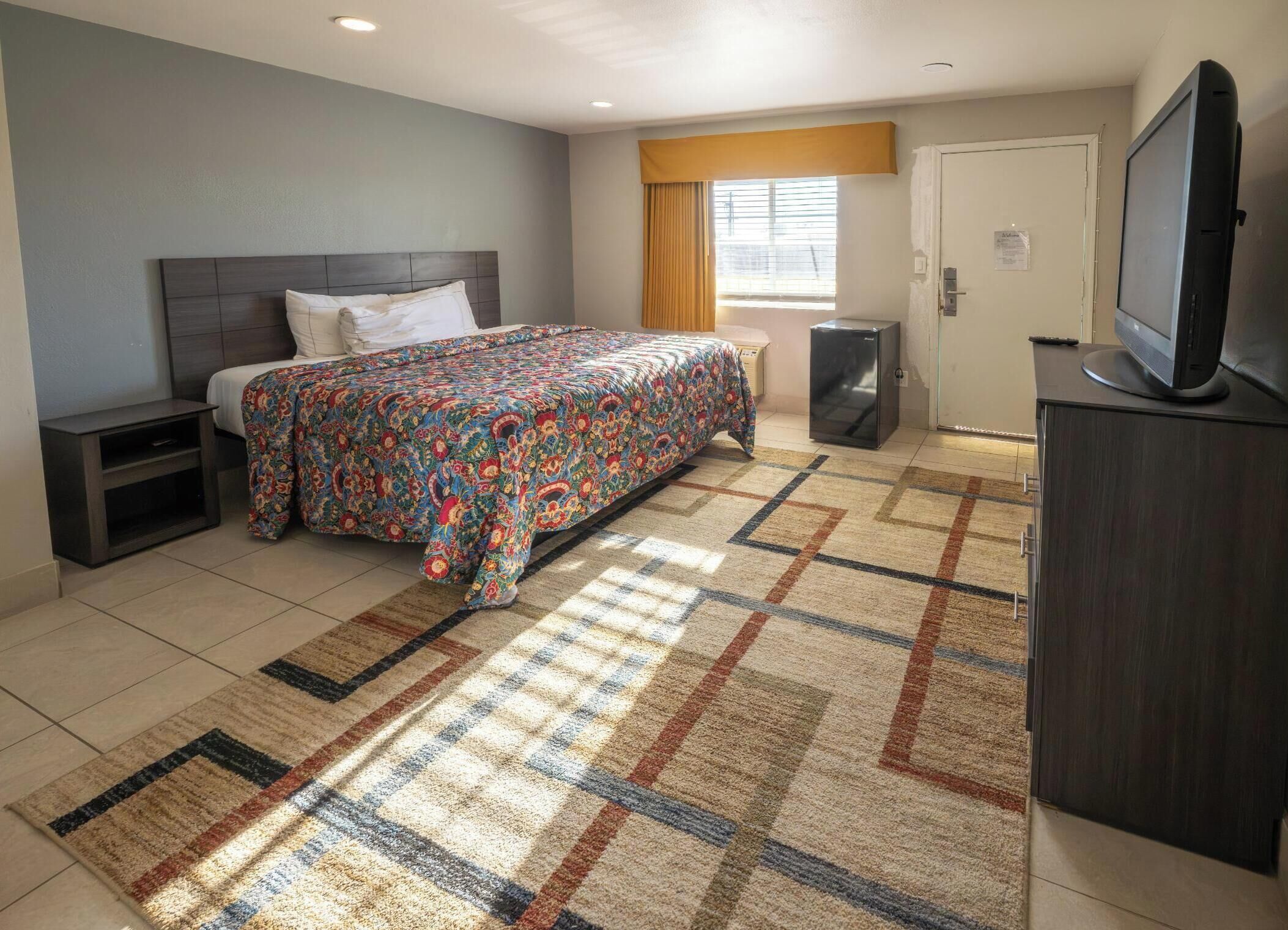 A hotel room with a bed, a TV, a small refrigerator, and a window with curtains.