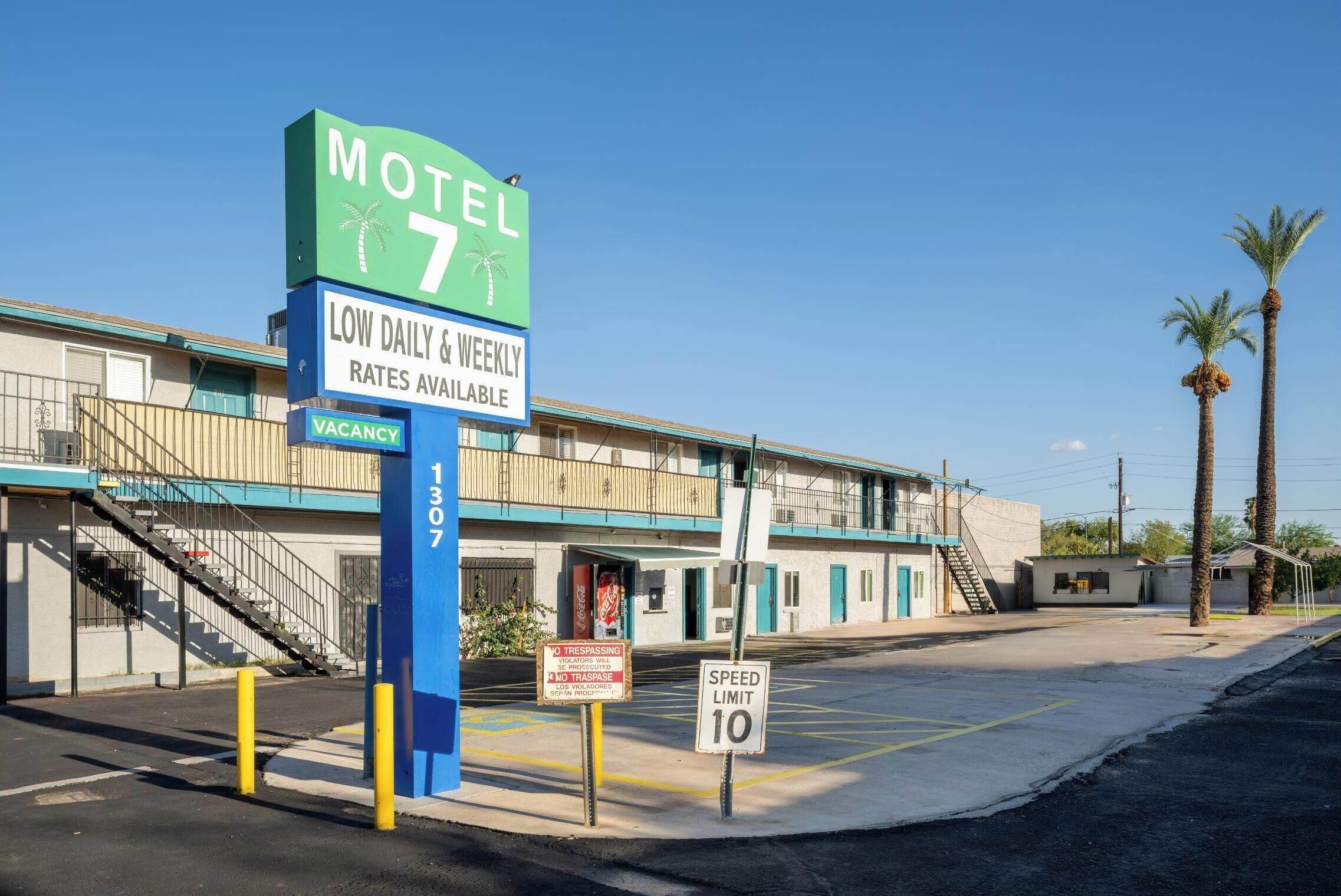 A motel with a sign indicating low daily and weekly rates, a vacancy sign, and a speed limit sign.