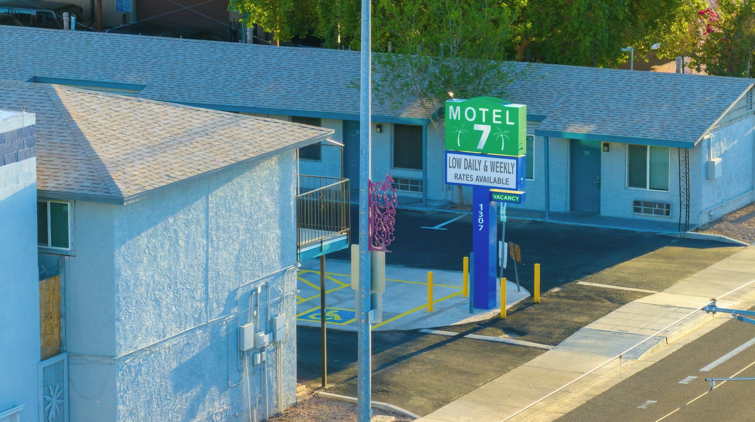 Un motel con un letrero verde que indica el número 7. Hay un estacionamiento con espacios delimitados y una plaza reservada para personas con discapacidad.