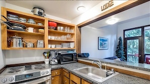 A kitchen with wooden cabinets, a stainless steel sink, a microwave, and a stove. - Snowater Condo - You'll be Sitting in the Lap of Luxury (Deming)