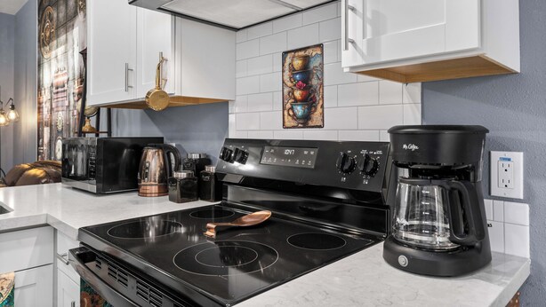 A modern kitchen with white cabinets, a black stove, a coffee maker, and a decorative wall piece.
