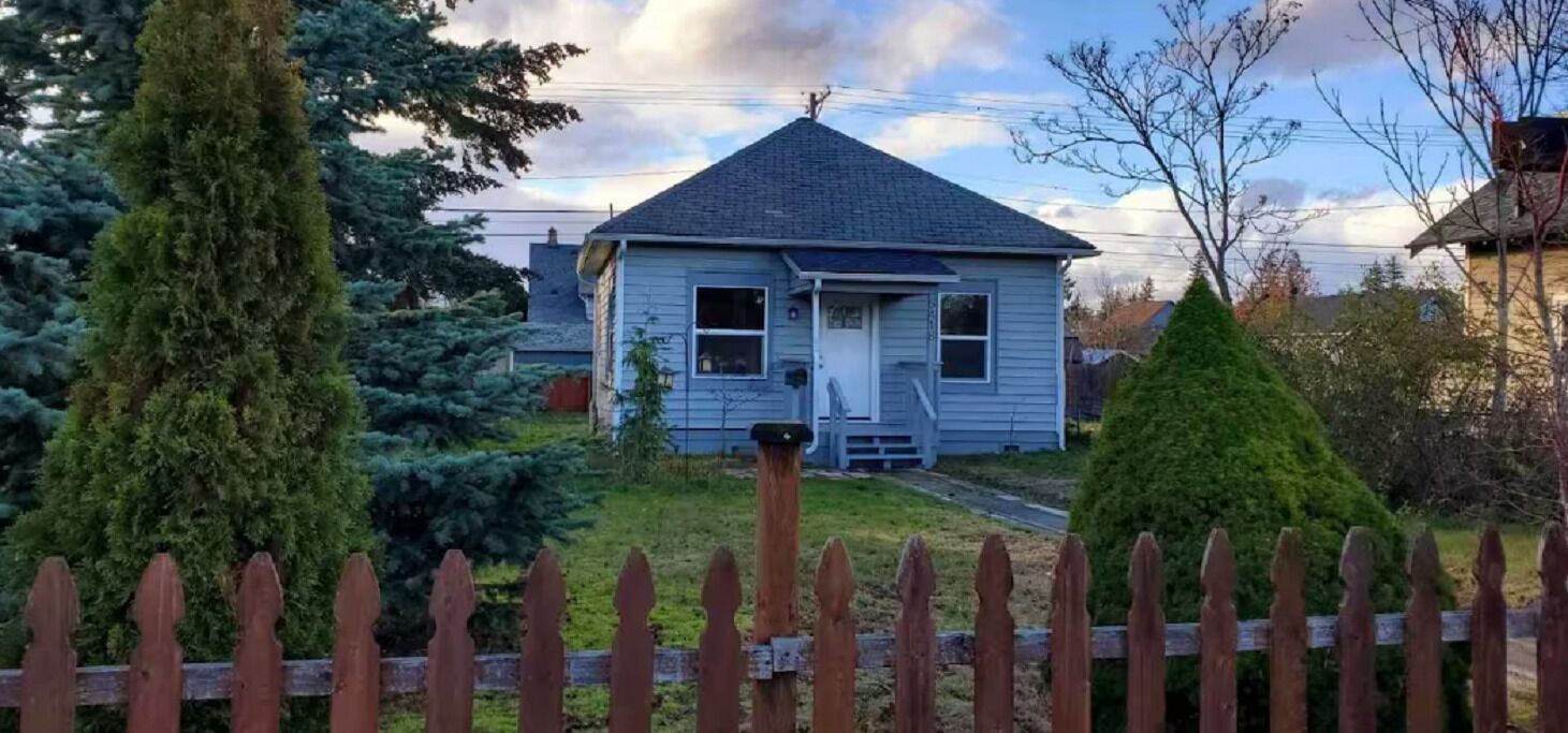 A single-story house with a gabled roof, a front porch, and a wooden picket fence.