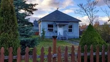 A single-story house with a gabled roof, a front porch, and a wooden picket fence.