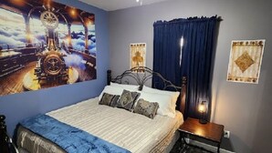 A bedroom with a bed, a ceiling fan, a nightstand, and a large wall mural.