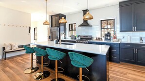 Una cocina moderna con armarios oscuros, una isla grande con taburetes de bar, electrodomésticos de acero inoxidable e iluminación colgante.