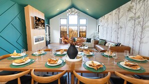 Un comedor con una mesa de madera dispuesta para seis personas, rodeada de sillas de madera. Un jarrón grande con hojas otoñales se encuentra en el centro.