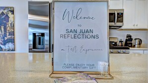 Une pancarte d’accueil pour l’hôtel San Juan Reflections, avec un cadeau offert et une petite carte contenant les coordonnées de l’établissement.