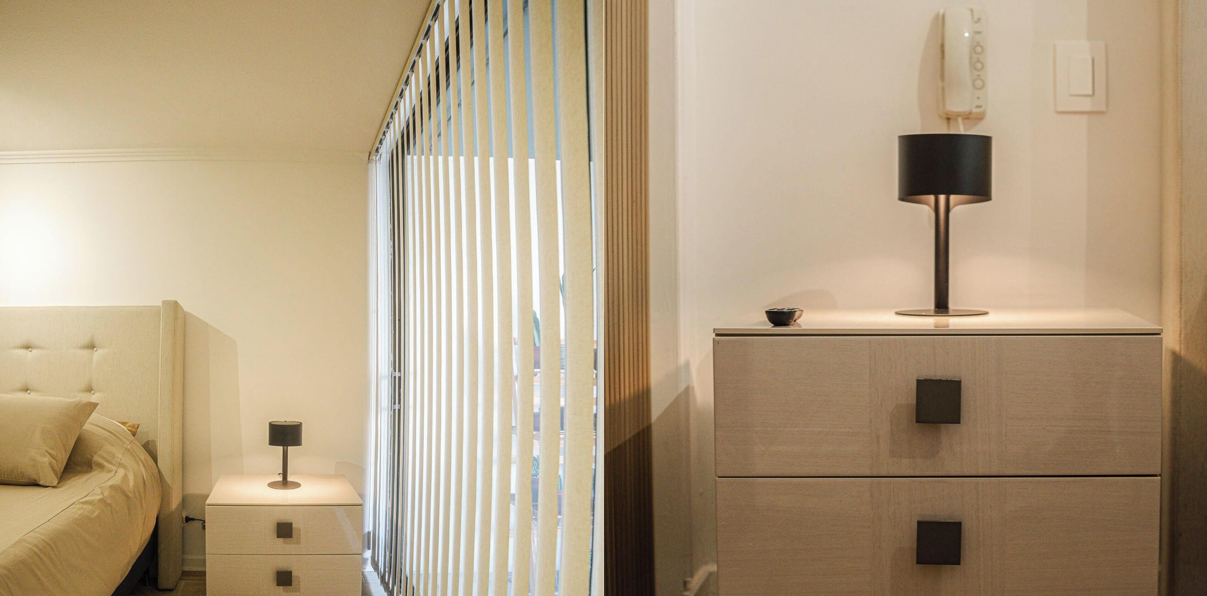 A bedroom with a bed, nightstand, lamp, and a wall-mounted heater.