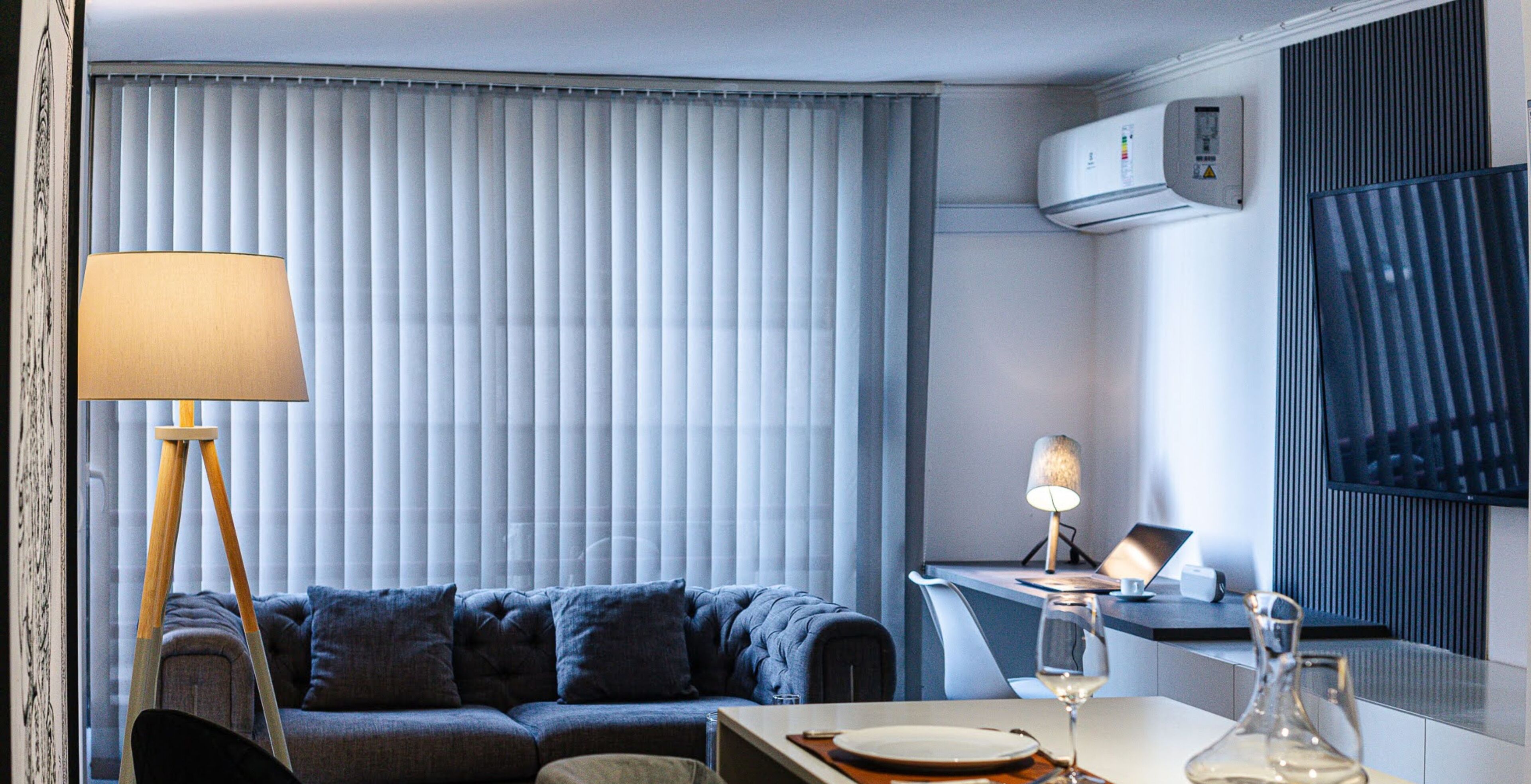 Ein modernes Hotelzimmer mit einer Couch, einem Esstisch mit einem Weinglas, einer Lampe und einer Klimaanlage.