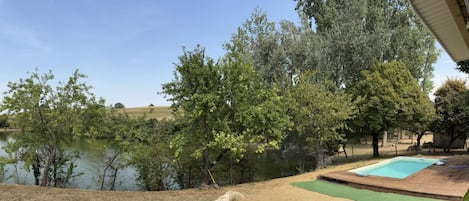 Vista de un lago con árboles y una terraza de madera con piscina.