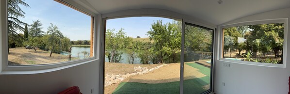 Ein Zimmer mit einer gebogenen Glastür, die zu einem Außenbereich mit See und Bäumen führt.