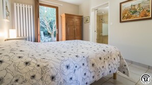A bedroom with a bed, a wooden wardrobe, a door leading outside, and a framed painting on the wall. - Home Sweet Lauragais (MAUREMONT)