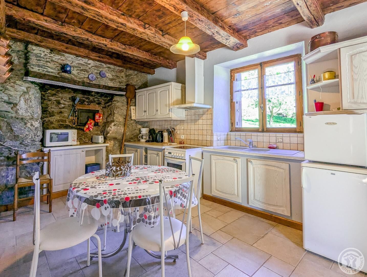 Una cocina rústica con paredes de piedra, vigas de madera, una mesa redonda con sillas y un ventanal con vistas.