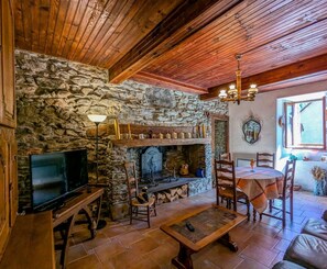 A rustic living room with stone walls, a fireplace, wooden furniture, and a television. - Maison Madon - Oô - Gîte (Oô)
