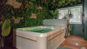 Un espacio de spa con hidromasaje, abundante follaje verde y una ventana con vistas.