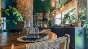 Un coin repas avec une table ronde dressée pour quatre personnes, un grand tronc d’arbre et diverses plantes.