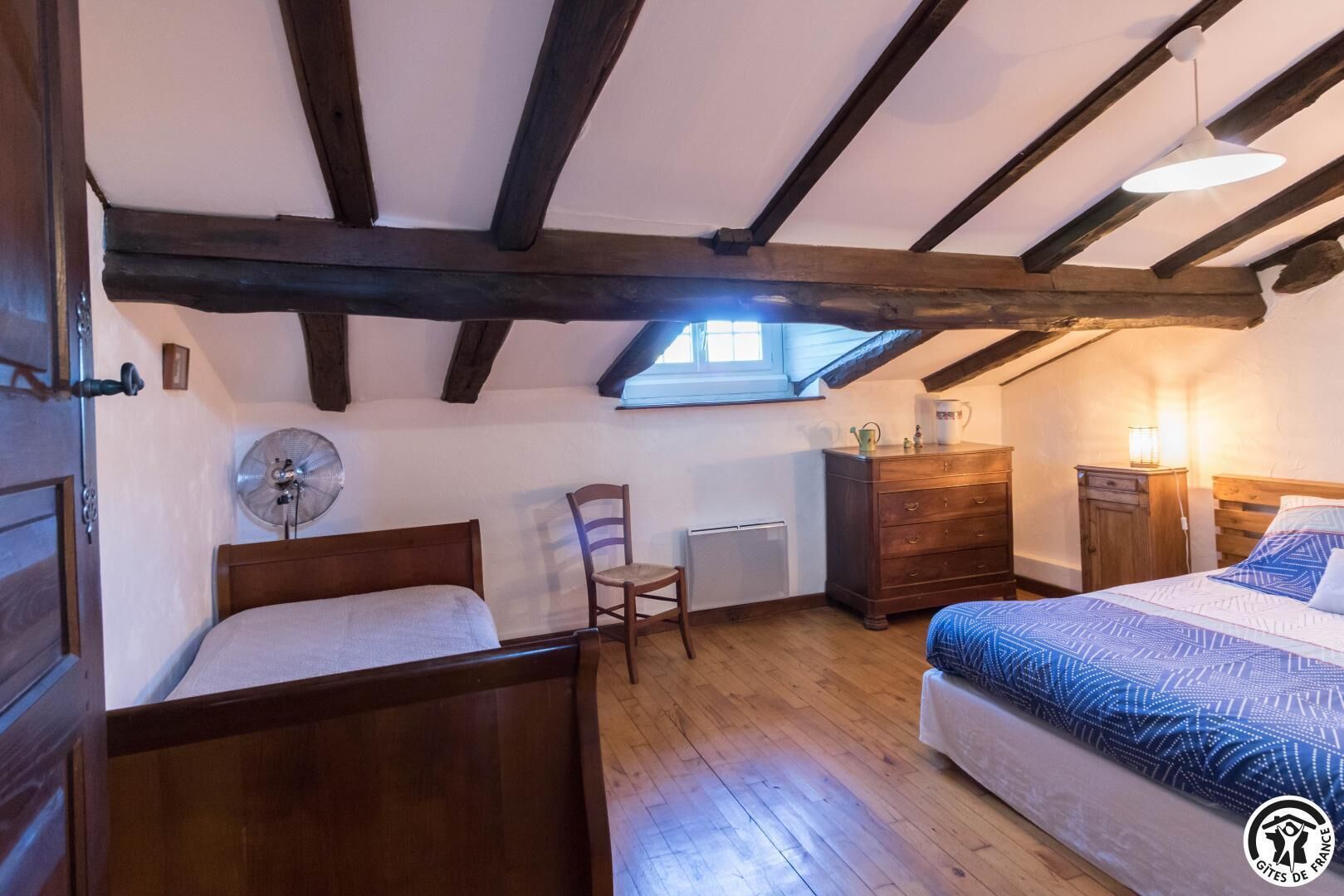 A bedroom with two wooden beds, a chair, a dresser, and a radiator.