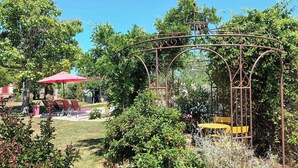 A garden with a metal gazebo, outdoor seating, and a red umbrella. - En Pouillac - SAINT THOMAS (SAINT THOMAS)