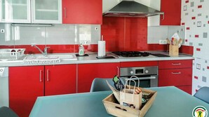 A modern kitchen with red cabinets, a stainless steel range hood, and a wooden table with a basket of bread. - Gaoudens - Soueich - Gîte (Soueich)