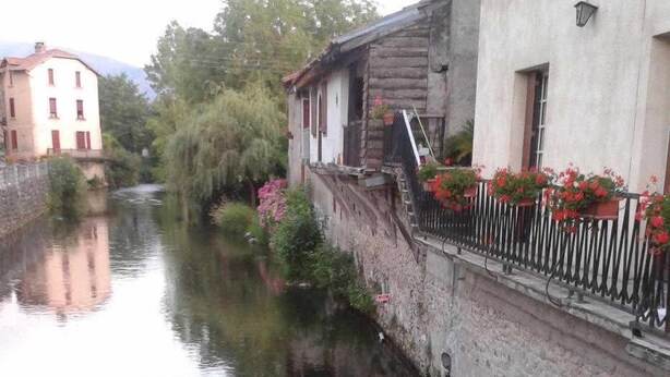 A canal with buildings on either side, a wooden house with a balcony, and red flowers in the foreground. - Gaoudens - Soueich - Gîte (Soueich)