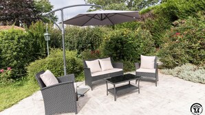 Un patio al aire libre con mobiliario de mimbre, una mesa y un paraguas grande.