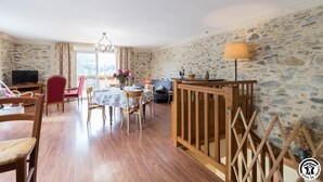 Una habitación con pared de piedra, suelo de madera, una mesa de comedor con sillas, un televisor y un balcón con vistas.