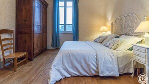 Ein Schlafzimmer mit Holzschrank, einem Einzelbett mit floralem Bettbezug, einem Nachttisch mit Lampe und einem Fenster mit blauen Vorhängen.
