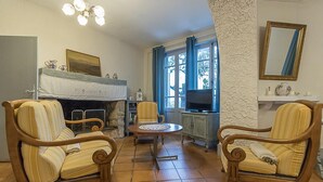 Ein gemütliches Wohnzimmer mit Kamin, zwei gestreiften Sesseln, einem kleinen runden Tisch und einem Fernseher.