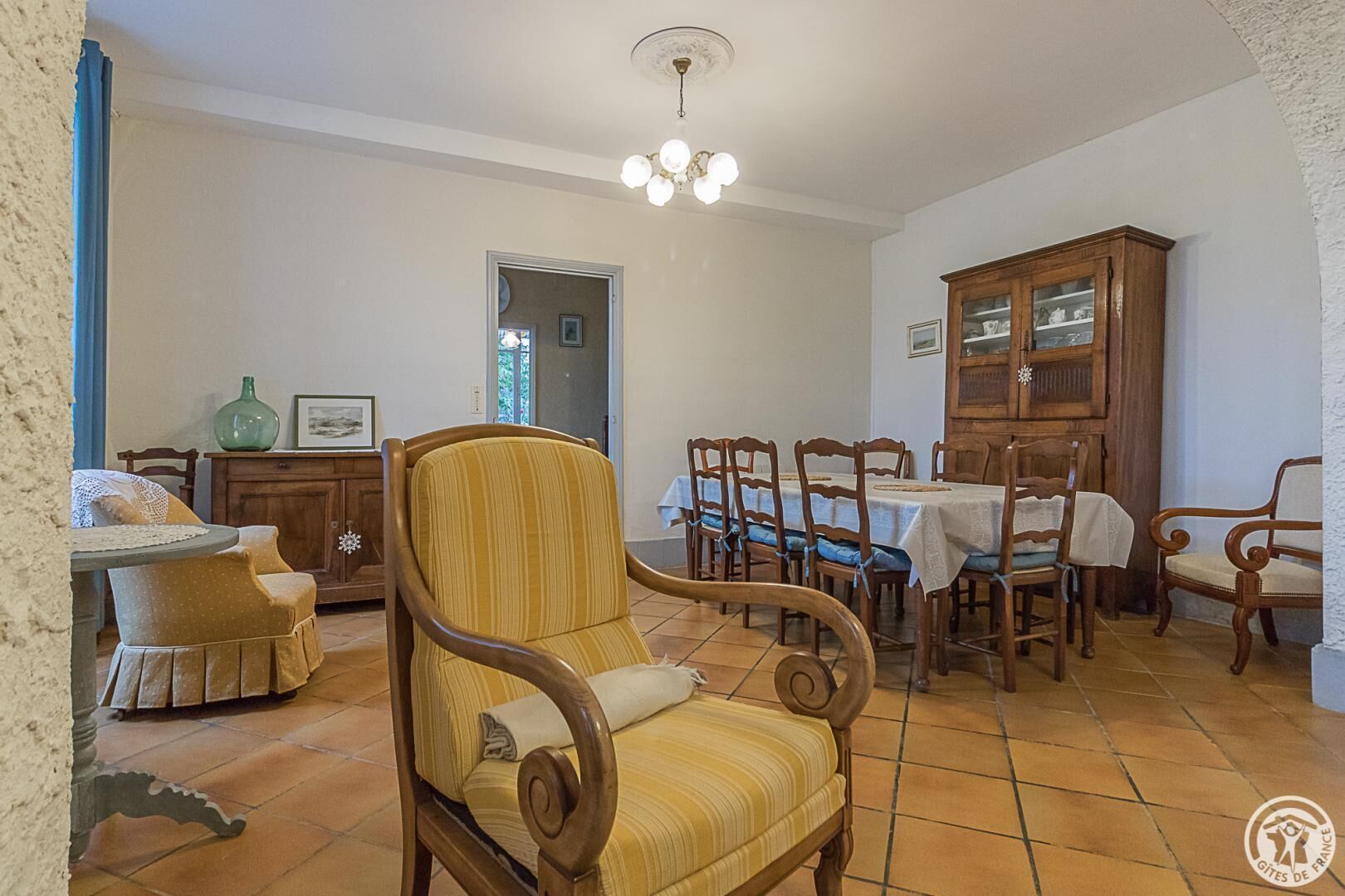 Un comedor con sillas de madera y una mesa, un armario con puertas de cristal y una araña.