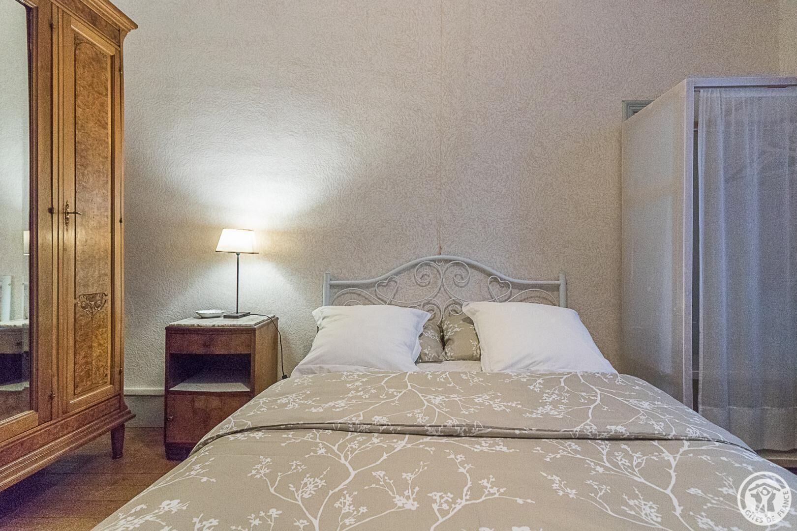 A bedroom with a bed, a nightstand, a lamp, and a wardrobe.