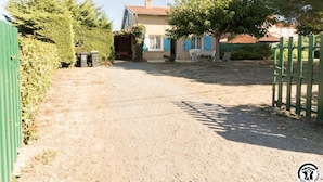 A residential property with a gravel driveway, a fenced yard, and a house with a red roof.