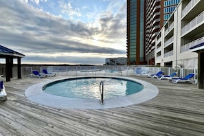 A pool area with a wooden deck, lounge chairs, and a tall building in the background. - Sugar Beach 133 ~ Great location, 2 Outdoor Pools, Free WiFi, Smart TV ~ Beach (Orange Beach)