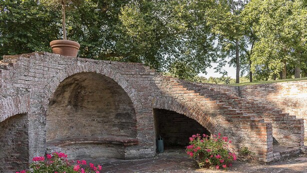 Un vieux pont en briques, doté d’une petite arche et agrémenté d’un élément décoratif aquatique en contrebas.