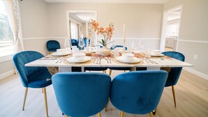 Une salle à manger avec une table rectangulaire dressée pour six personnes, des chaises bleues, des assiettes blanches et un vase rempli de fleurs.