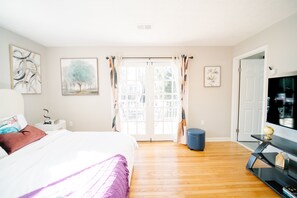 Quarto com cama, mesa de cabeceira, penteadeira, televisão e janela com cortinas.