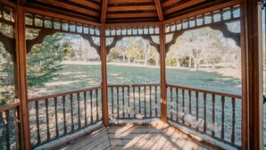 Un belvédère en bois, doté d’un plancher en bois et d’une balustrade, entouré d’arbres et d’herbe.