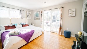 Une chambre avec un grand lit, un plancher en bois, un balcon avec vue et un meuble pour la télévision.