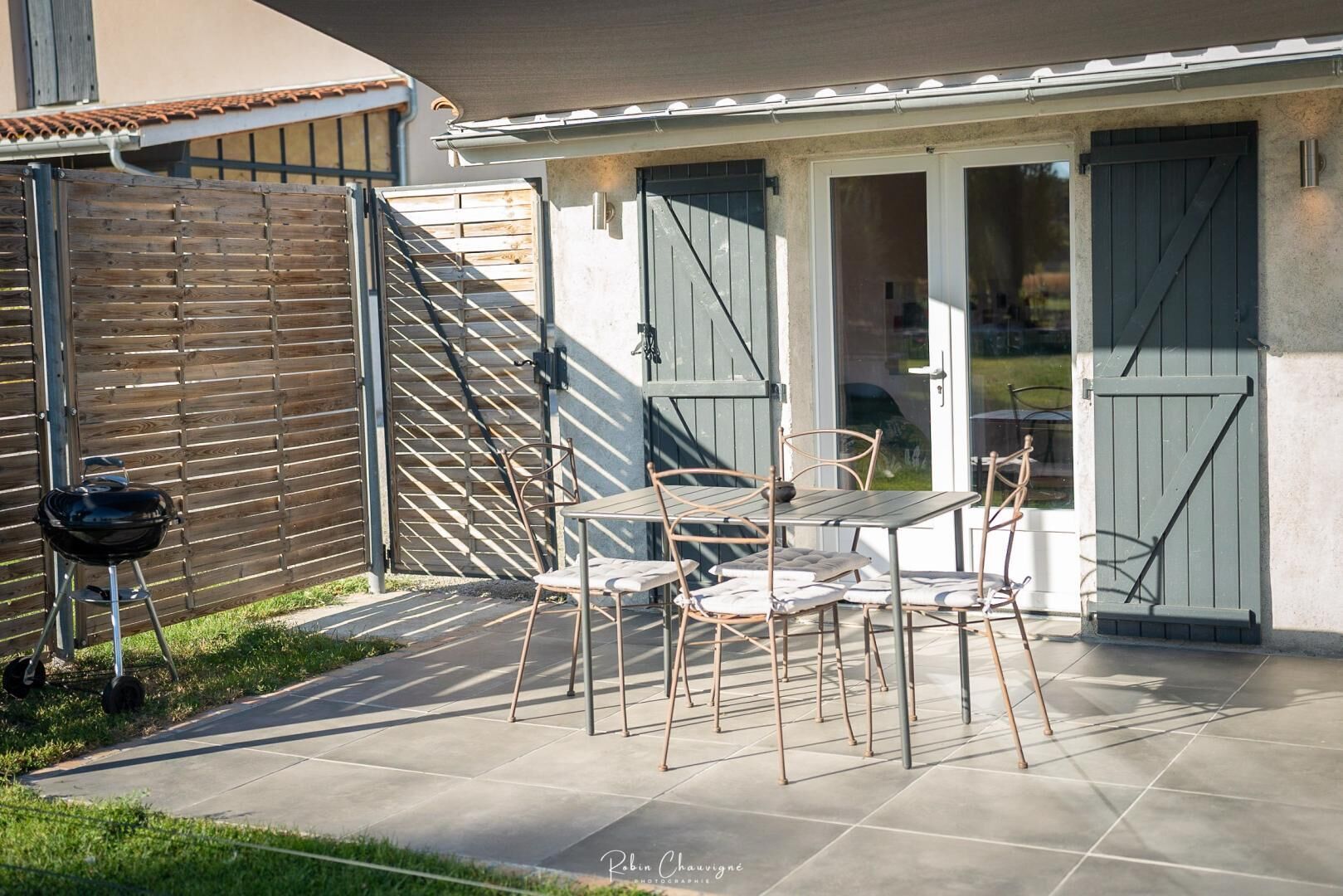 Un patio con mesa y sillas, una parrilla y una zona cubierta con puertas correderas.