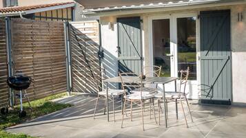 Un patio con mesa y sillas, una parrilla y una zona cubierta con puertas correderas.