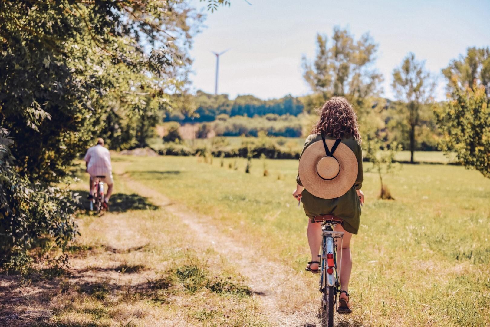 Eine Person fährt Fahrrad auf einem Feldweg, der von Grünflächen gesäumt wird.