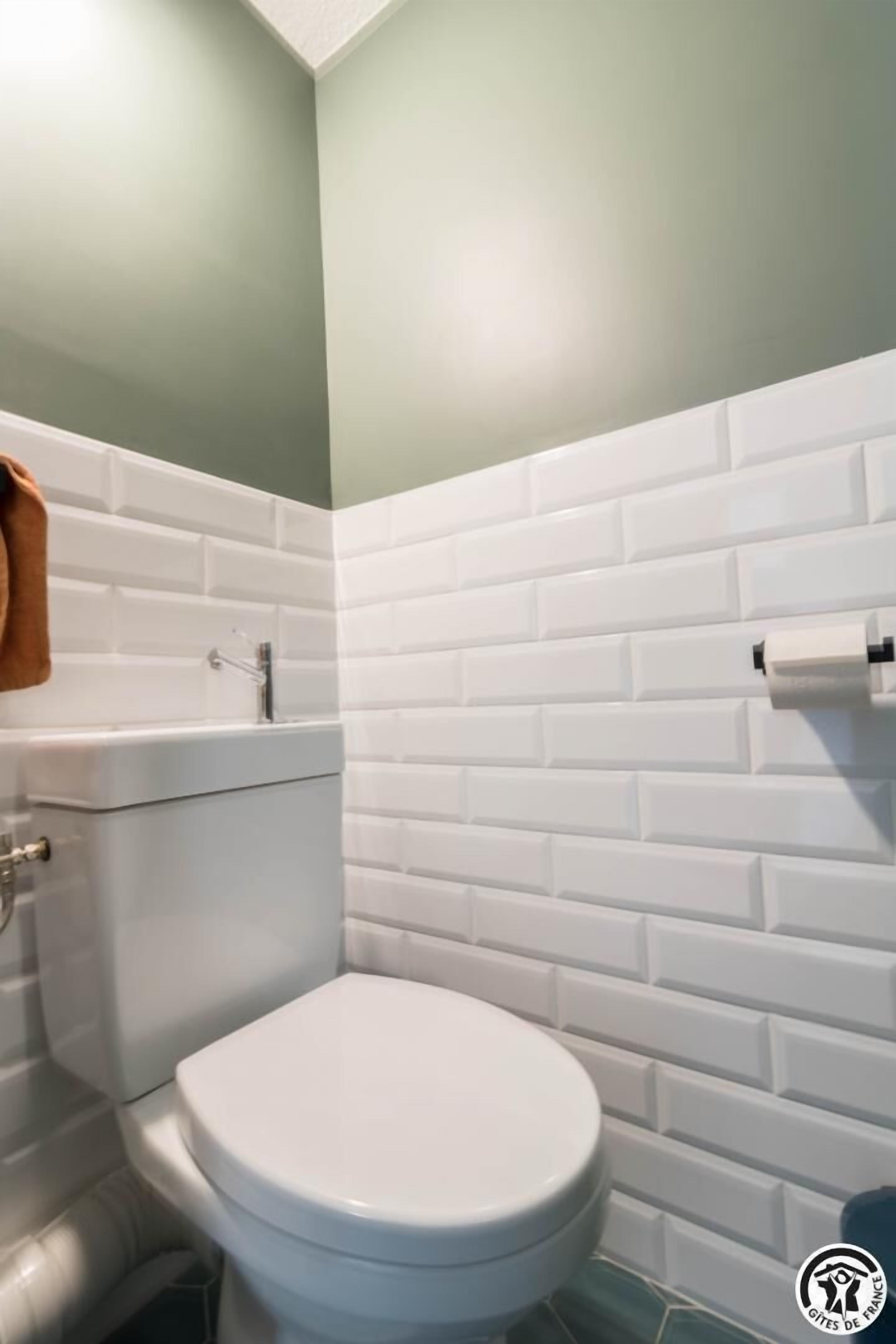 Un baño con inodoro blanco, paredes cubiertas de baldosas blancas y una pared de acento verde.