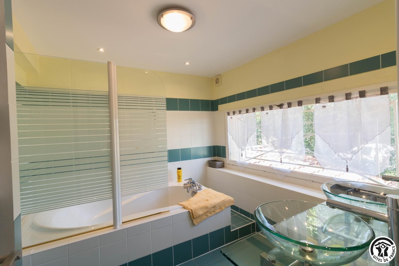 Ein modernes Badezimmer mit einem Waschbecken aus Glas, einer Badewanne und einem Fenster mit Jalousien.