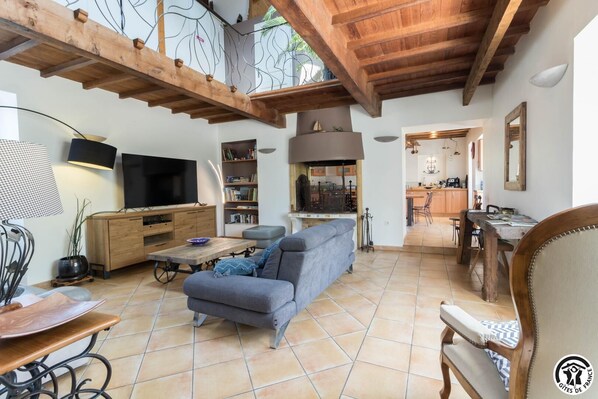A spacious living area with a sofa, TV, wooden cabinets, and a kitchen in the background.