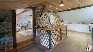A rustic interior with a stone wall, wooden ceiling, and a wooden counter with a clock.