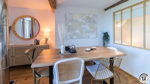 A modern dining area with a wooden table, two white chairs, a round mirror, and a wall-mounted abstract painting.