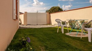 A backyard with a lawn, a white plastic chair, a table, and a white fence.